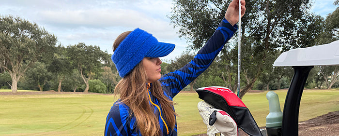 Female golfer selecting a club from her bag and wearing the winter visor in bright blue from swing out sister golf