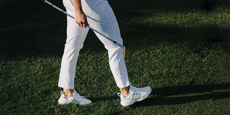 Close up of a woman golfer's legs walking to the next shot wearing white adidas golf  7/8 cropped length trousers