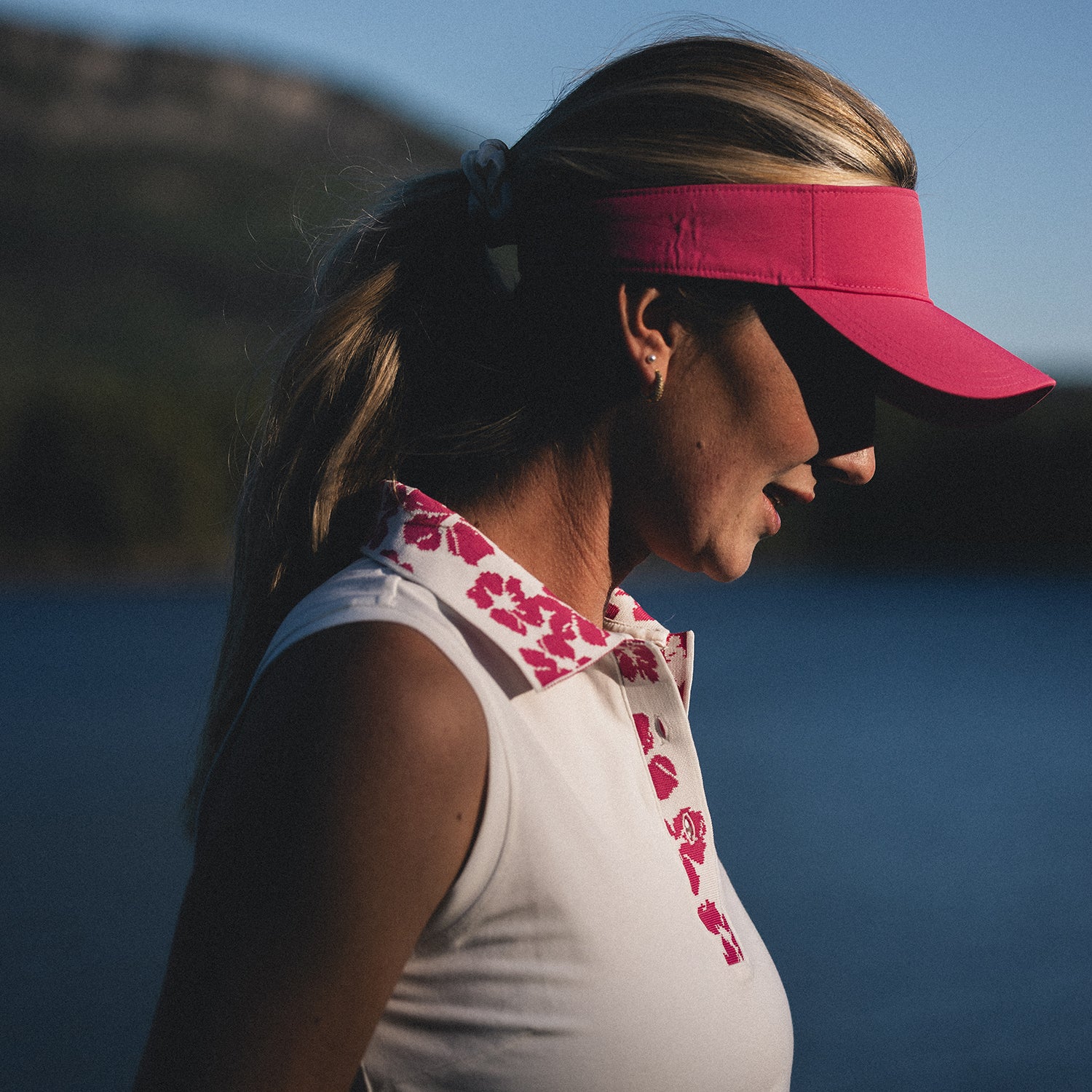 Close up of golfer wearing a puma golf visor and Puma Golf white Ladies Cotton Blend Sleeveless Polo with pink hibiscus print collar