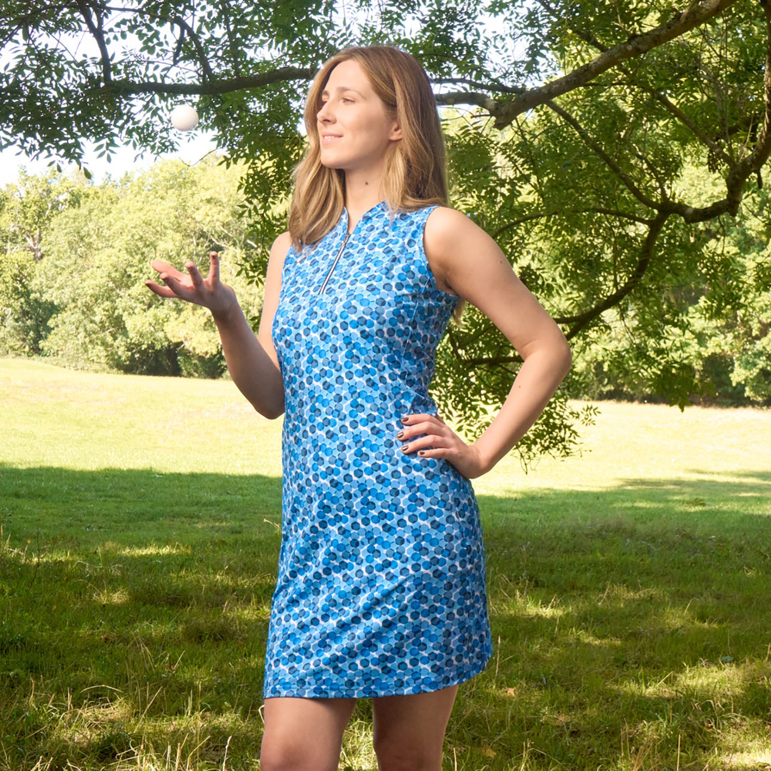 Golfer with a golf ball under a tree at a golf course wearing Pure Golf Sleeveless Dress in blue Abstract Geometric Print