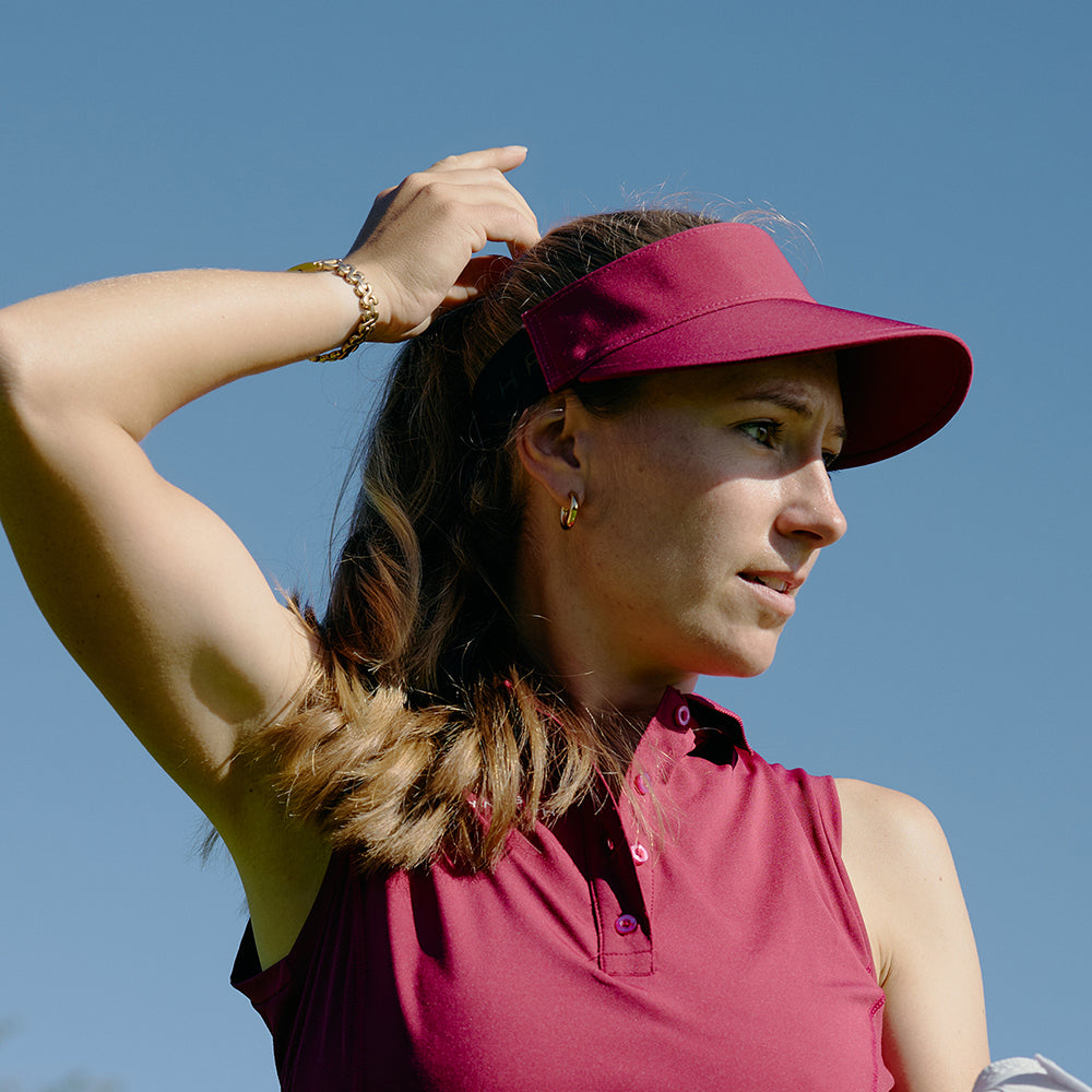 Female gofer wearing a Rohnisch Ladies Rasberry colour Visor with Adjustable Fit for Sport-Luxe Style with a blue sky background.