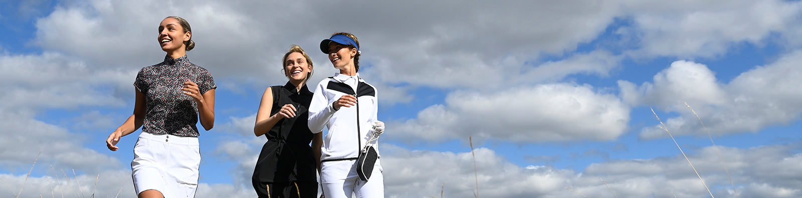 Three female golfers wearing coordinating monochrome outfits with a blue sky with white clouds background.