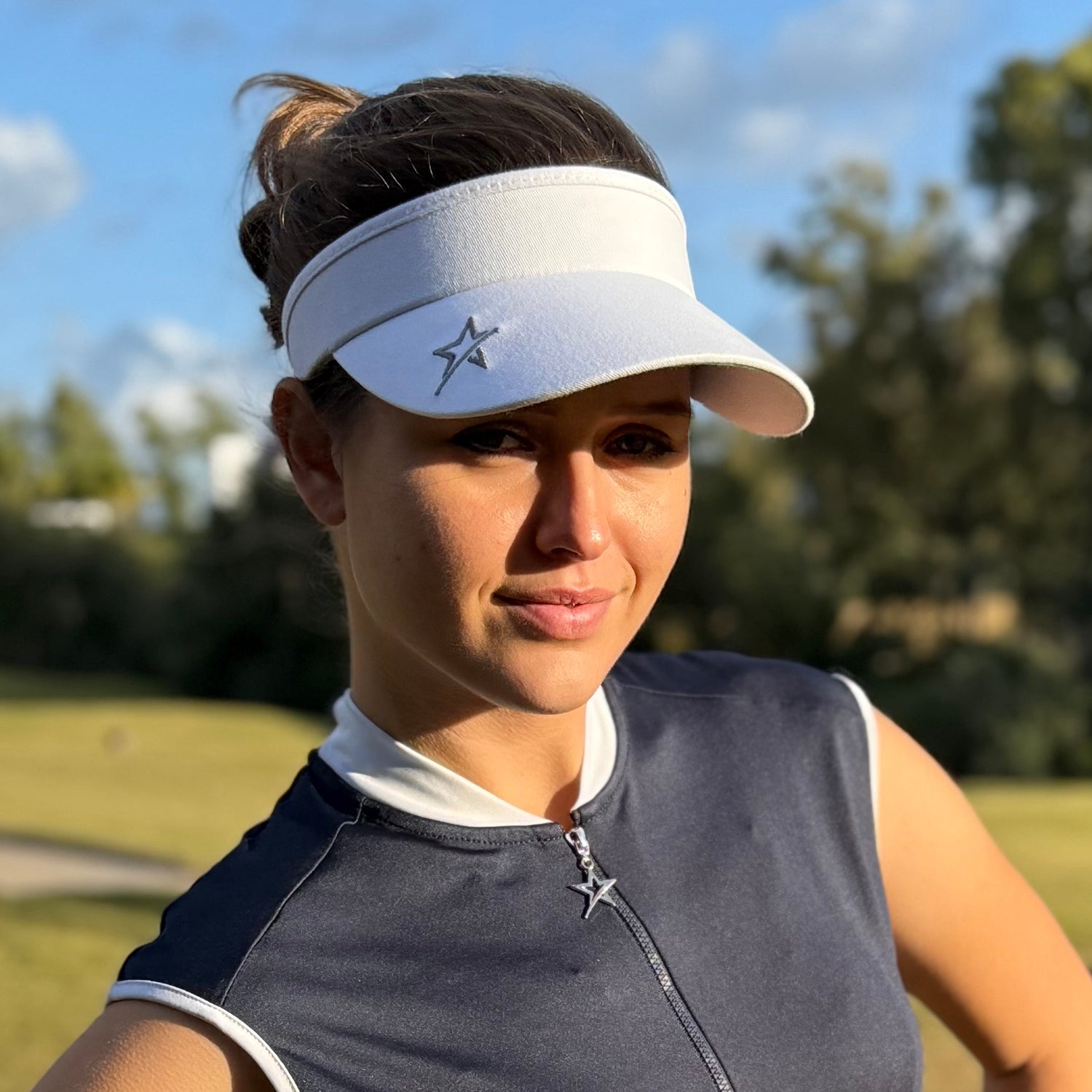 Woman wearing a white visor from Swing Out Sister on a golf course. Available at GolfGarb.